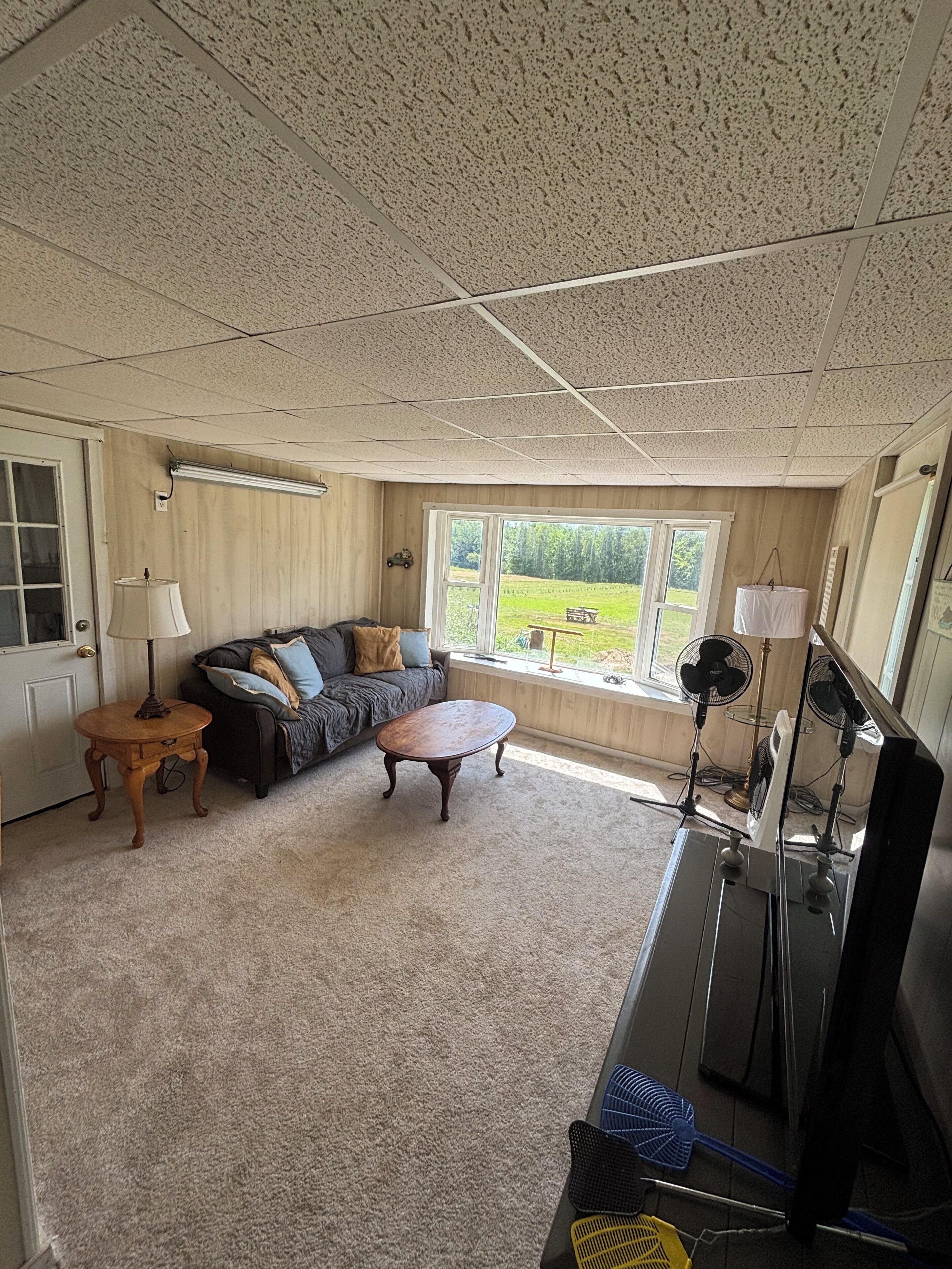 A living room with a sectional sofa, a coffee table, and a television. There is a window providing a view of a grassy area.