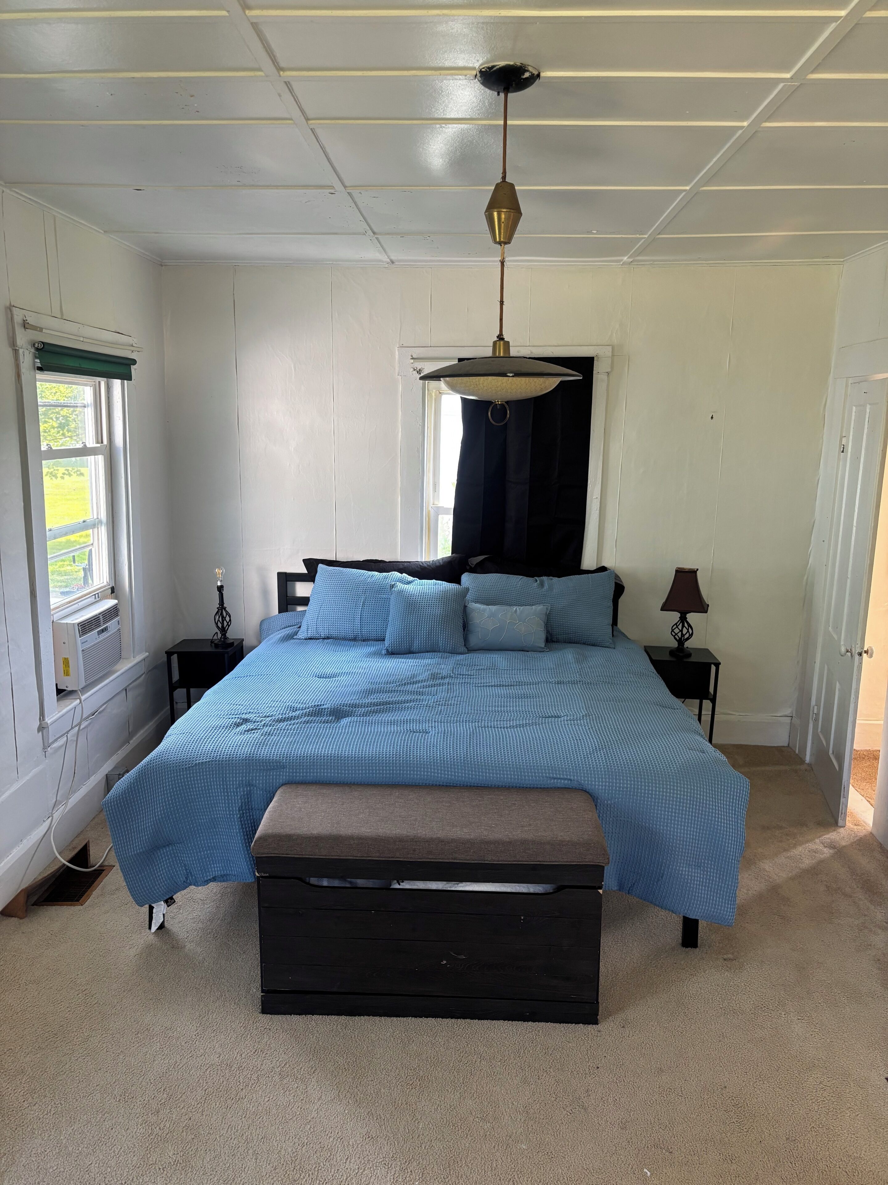 A bedroom with a bed, bedside tables, a hanging light fixture, and a window with curtains.