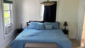 A bedroom with a bed, bedside tables, a hanging light fixture, and a window with curtains.