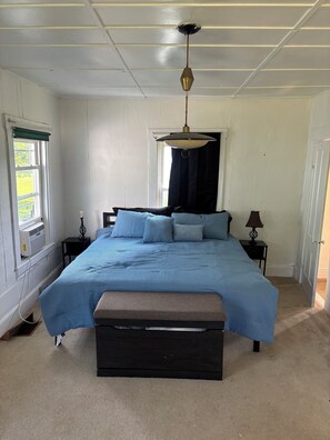 Un dormitorio con cama, mesitas de noche, lámpara colgante y ventana con cortinas.