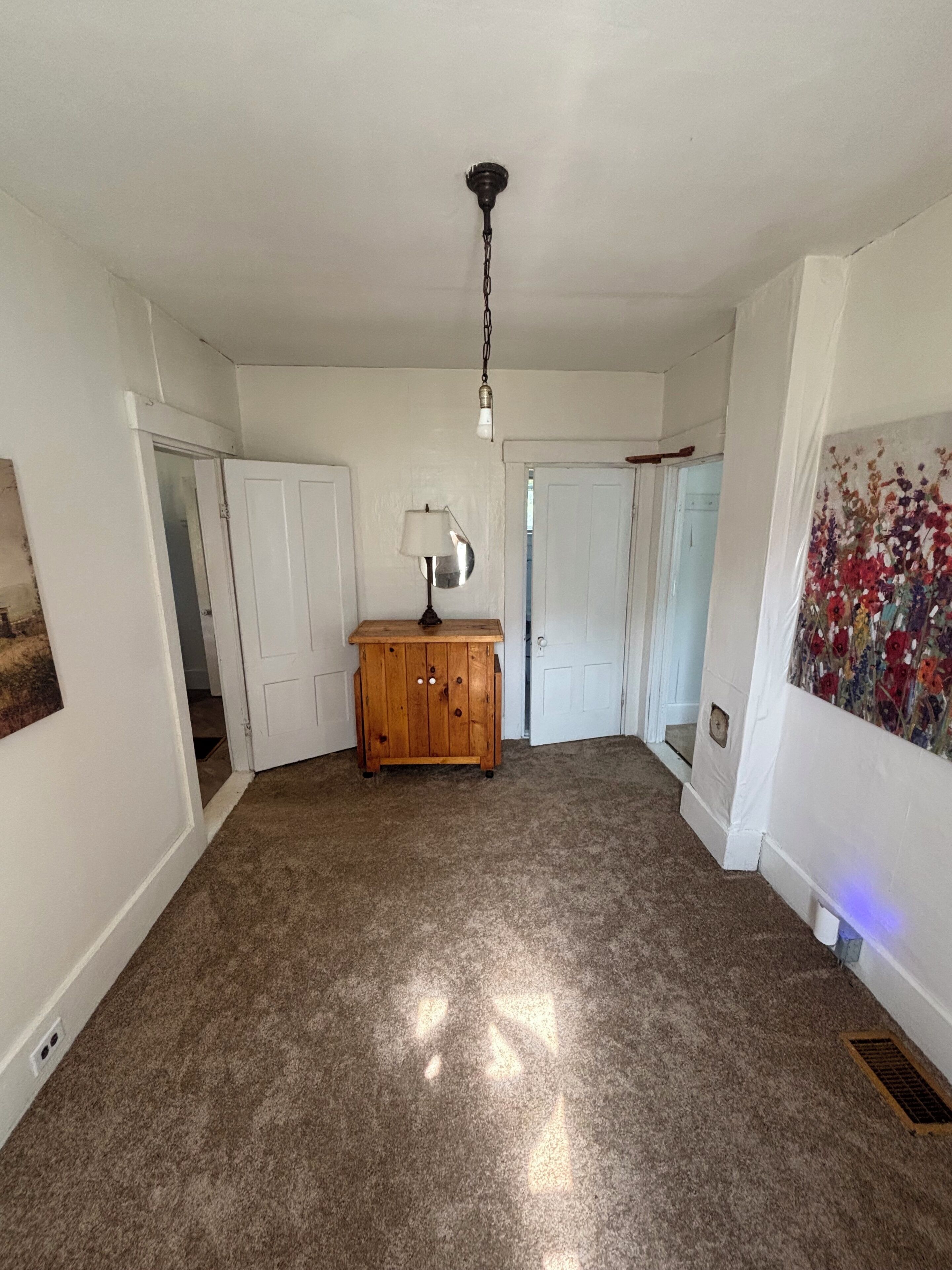 A room with carpeted flooring, a wooden cabinet, a lamp, and a ceiling light fixture.