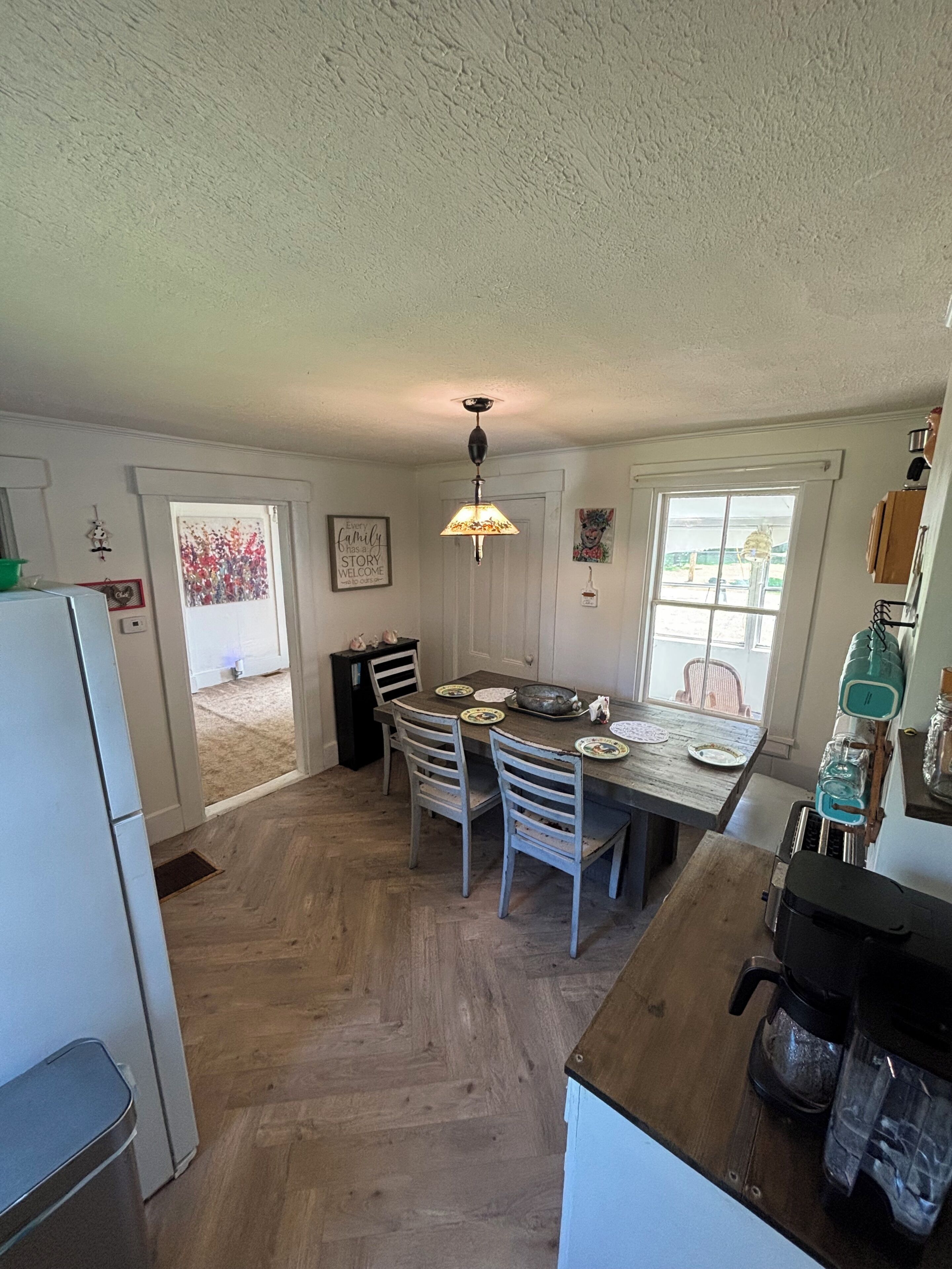 A kitchen with a dining table, chairs, a refrigerator, and a window.