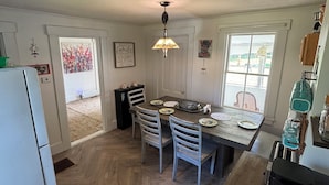 A kitchen with a dining table, chairs, a refrigerator, and a window.
