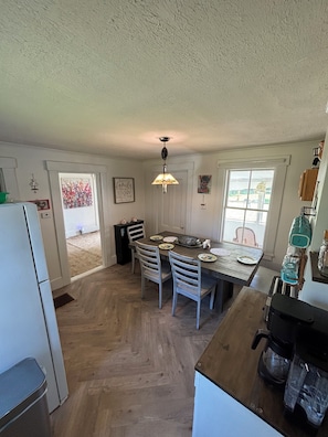 A kitchen with a dining table, chairs, a refrigerator, and a window. - Unplug at Gentle Giant Acres — Historic Maine Farmhouse on 16 Acres (Kingman)