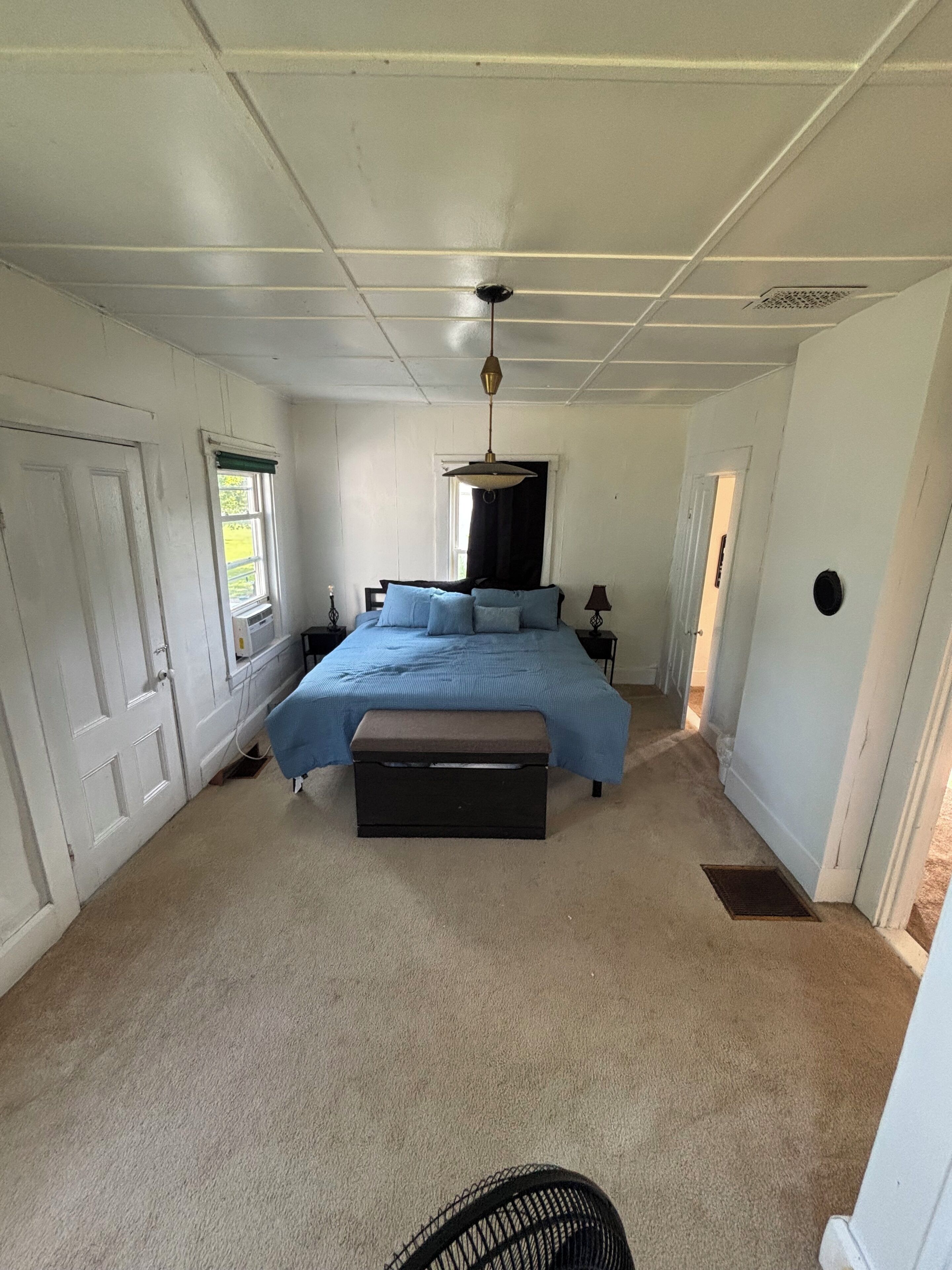 A bedroom with a bed, a bench, a window, and a door.