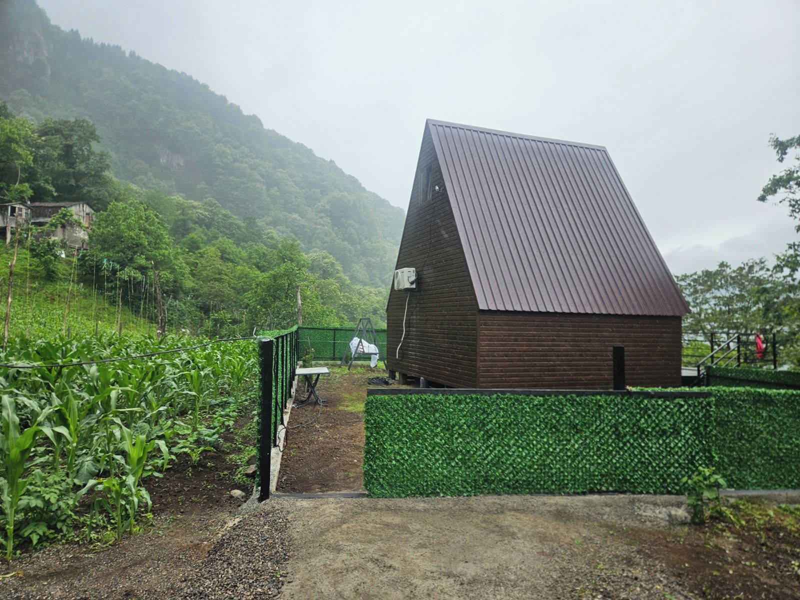 Un edificio rústico con techo inclinado, rodeado de vegetación exuberante y montañas al fondo.