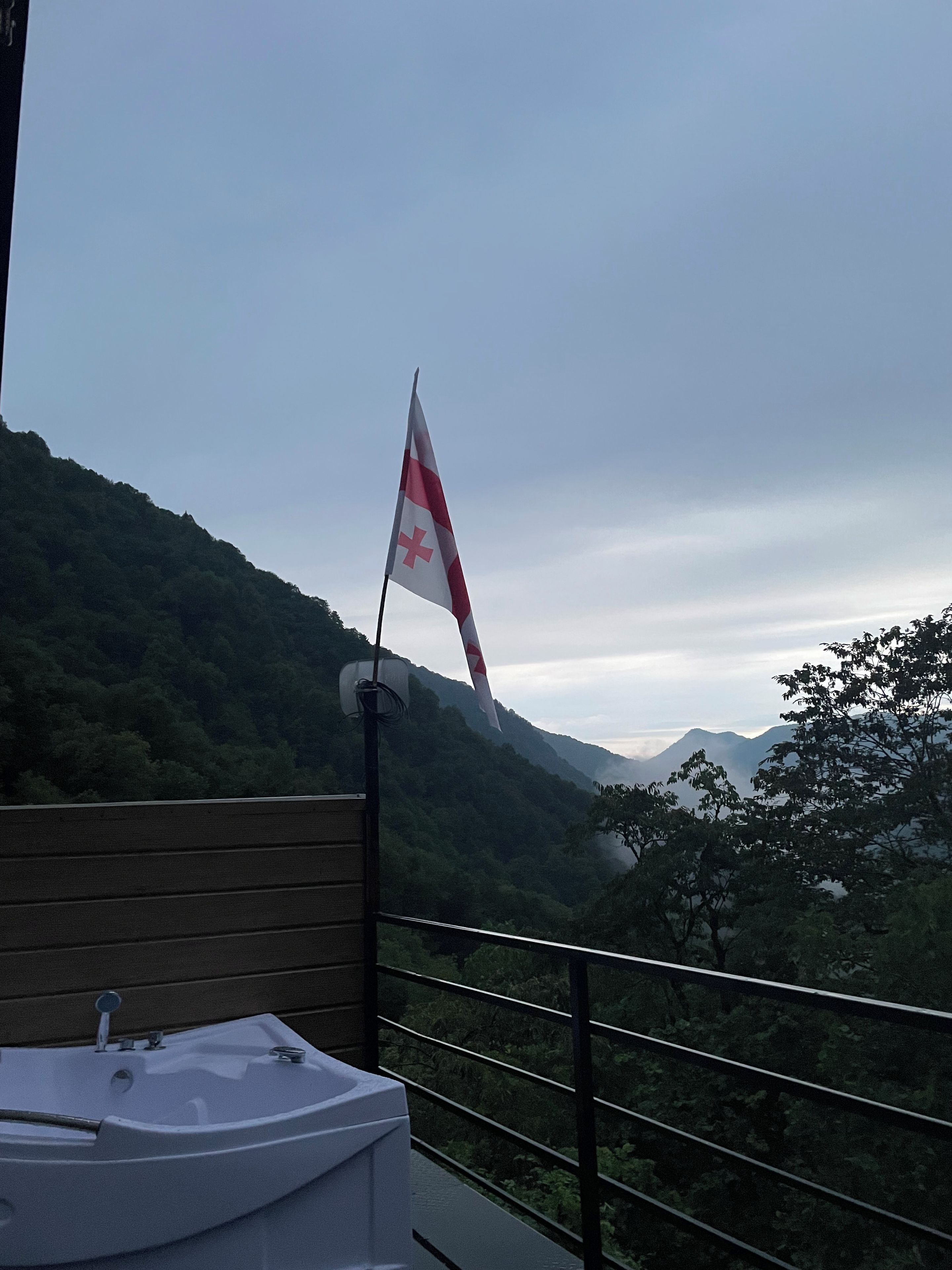 Una bandera en un asta, una barandilla de madera y un paisaje montañoso.