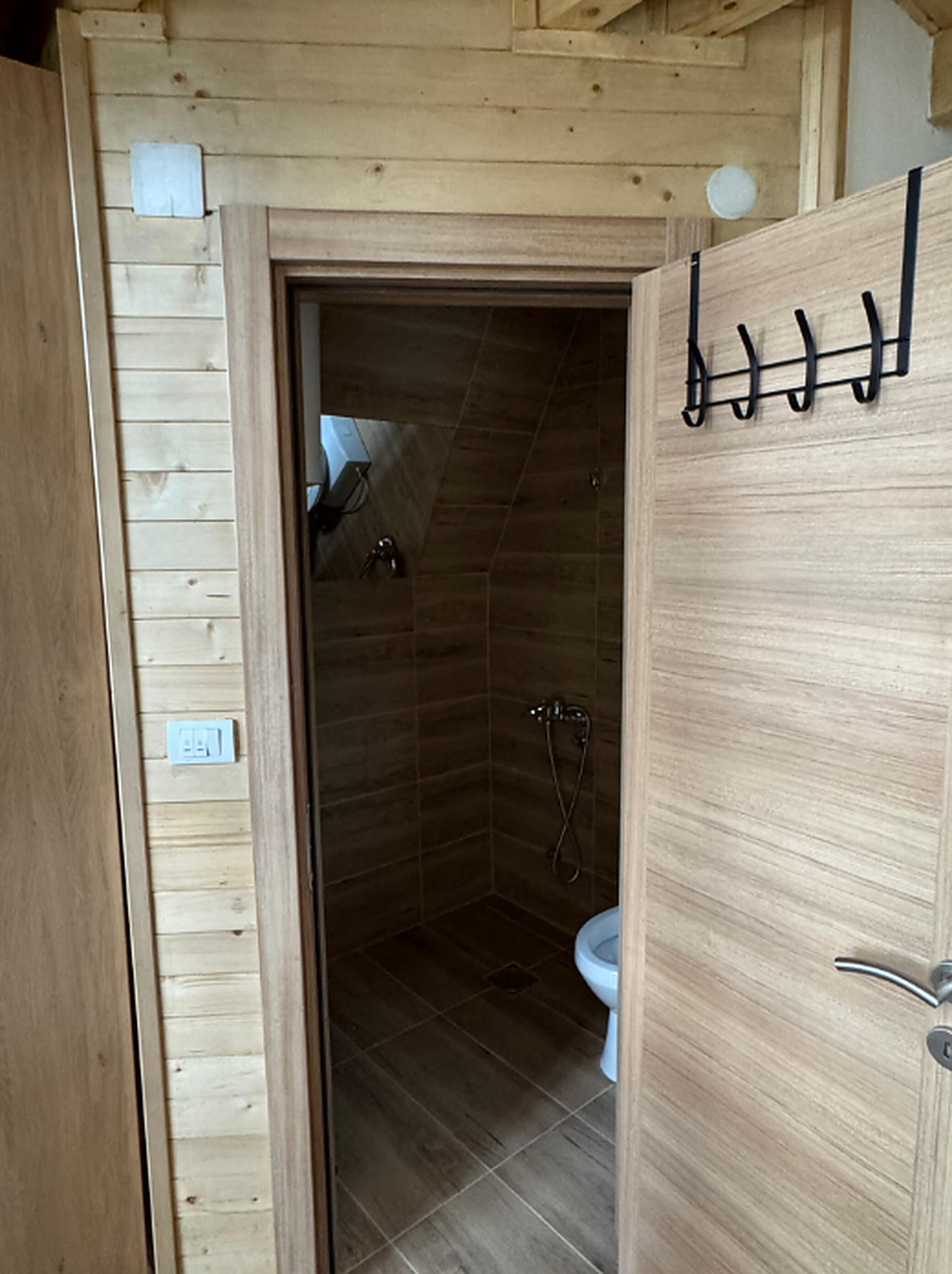 Un interior de madera con zona de ducha, inodoro y una puerta con ganchos.