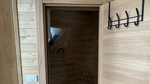 A wooden interior with a shower area, a toilet, and a door with hooks.