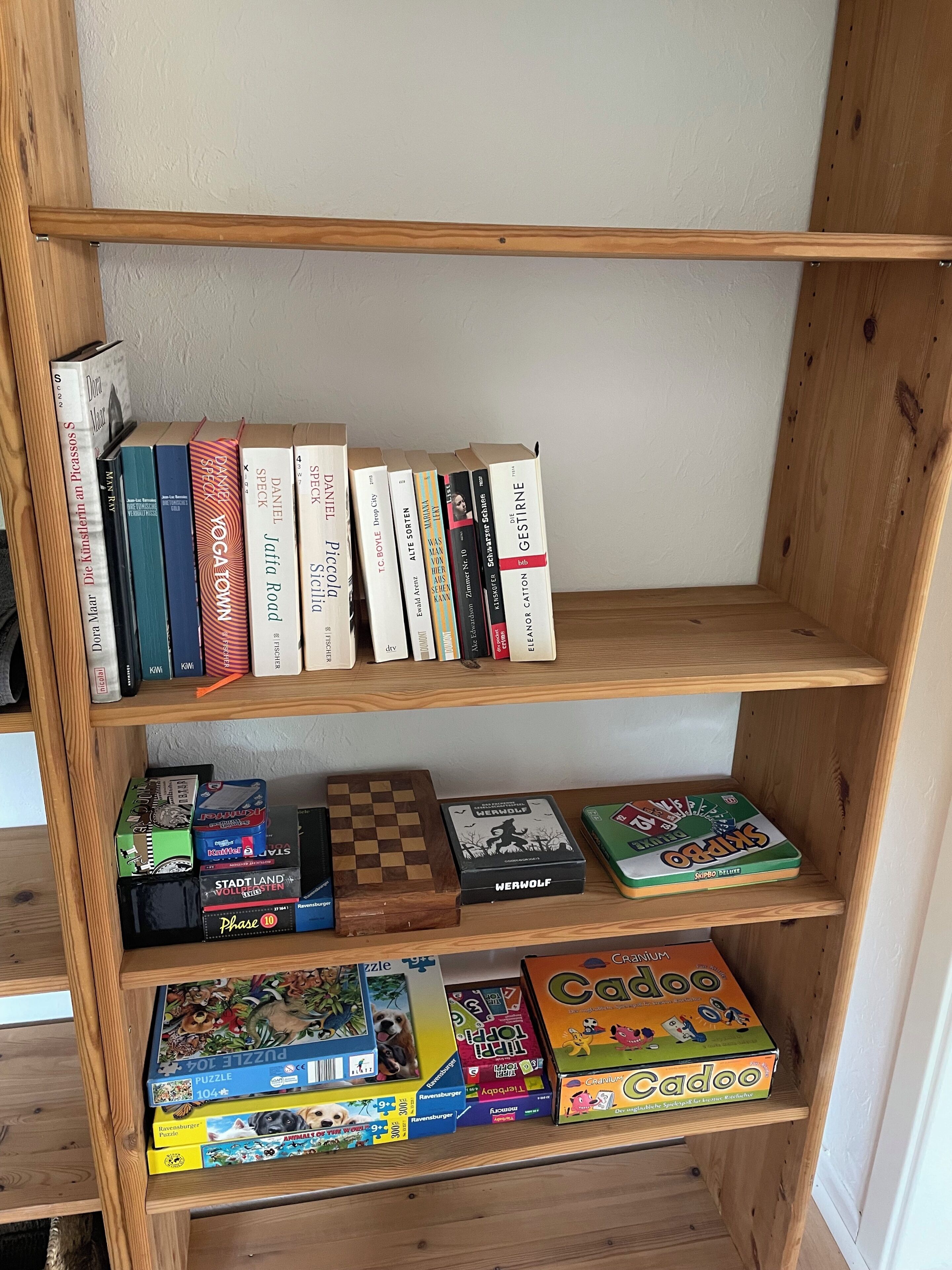 Une bibliothèque en bois contenant divers livres et jeux de société.
