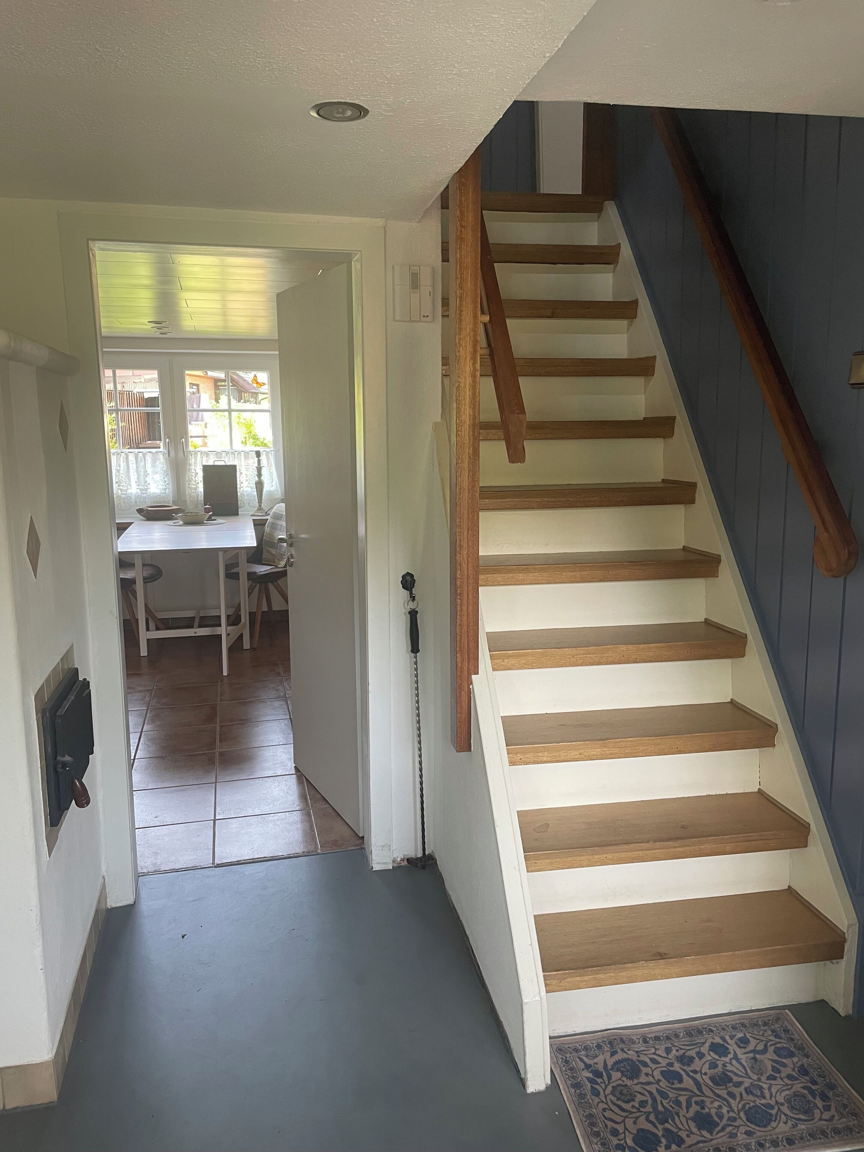 Un escalier avec des marches en bois menant à l’étage supérieur, une porte avec une poignée et un sol carrelé.