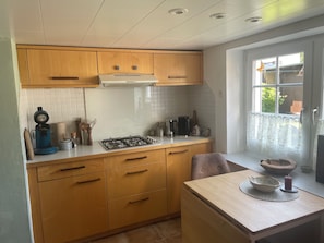 Une cuisine de taille réduite, dotée de meubles en bois, d’une cuisinière à gaz et d’une fenêtre donnant sur l’extérieur.