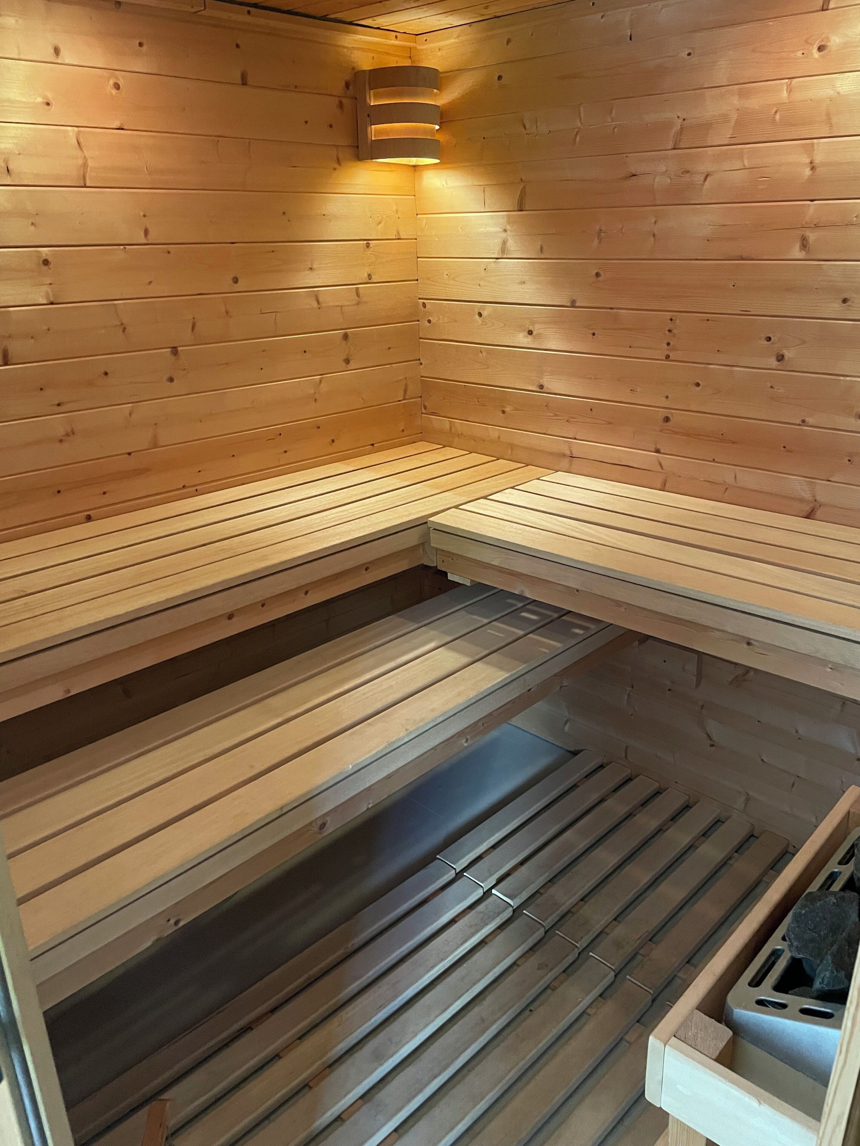 A sauna with wooden walls and benches, a ceiling light, and a stone basin.