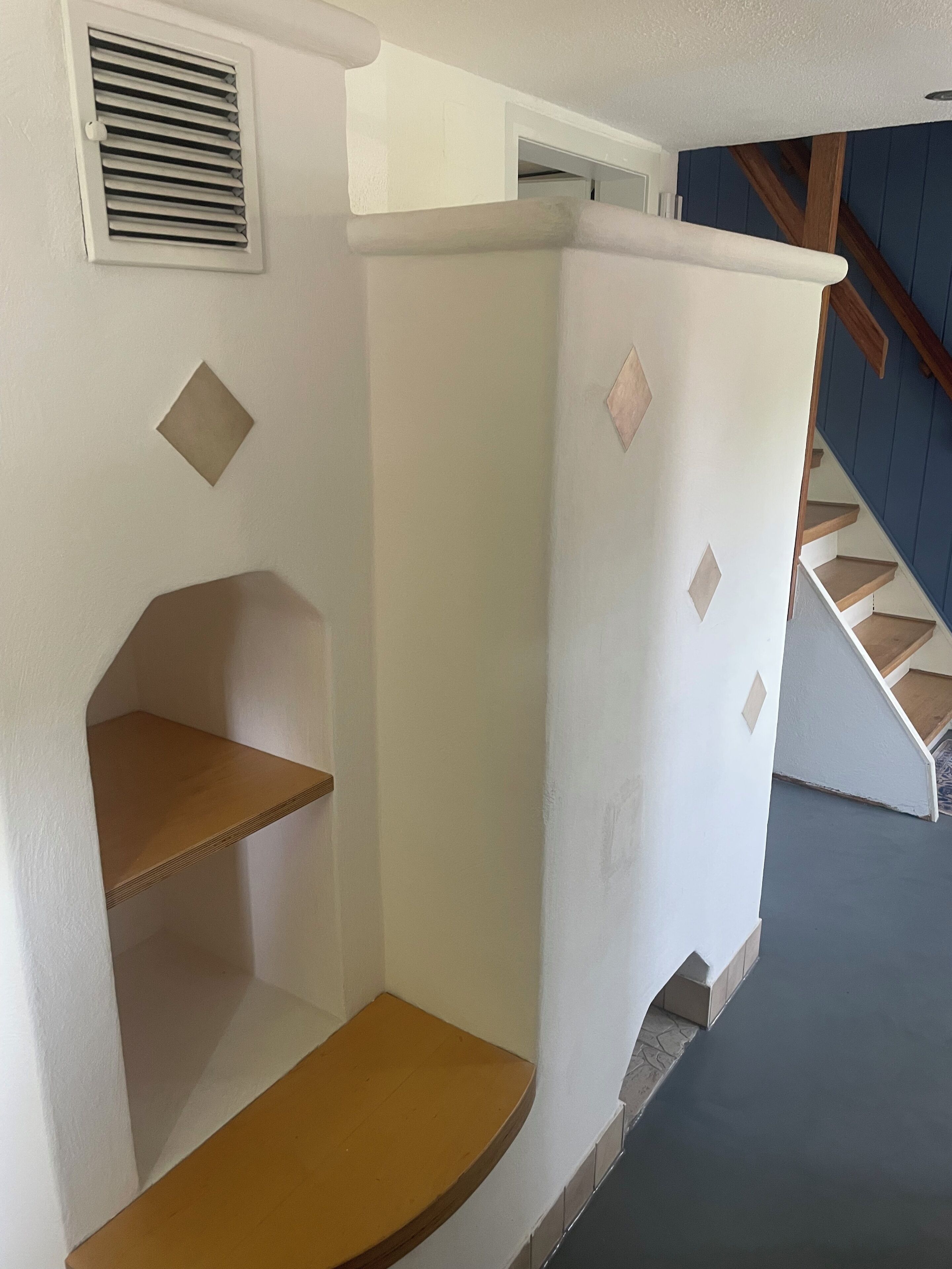 A corner of a room with a white wall, a wooden shelf, and a white door with a window.