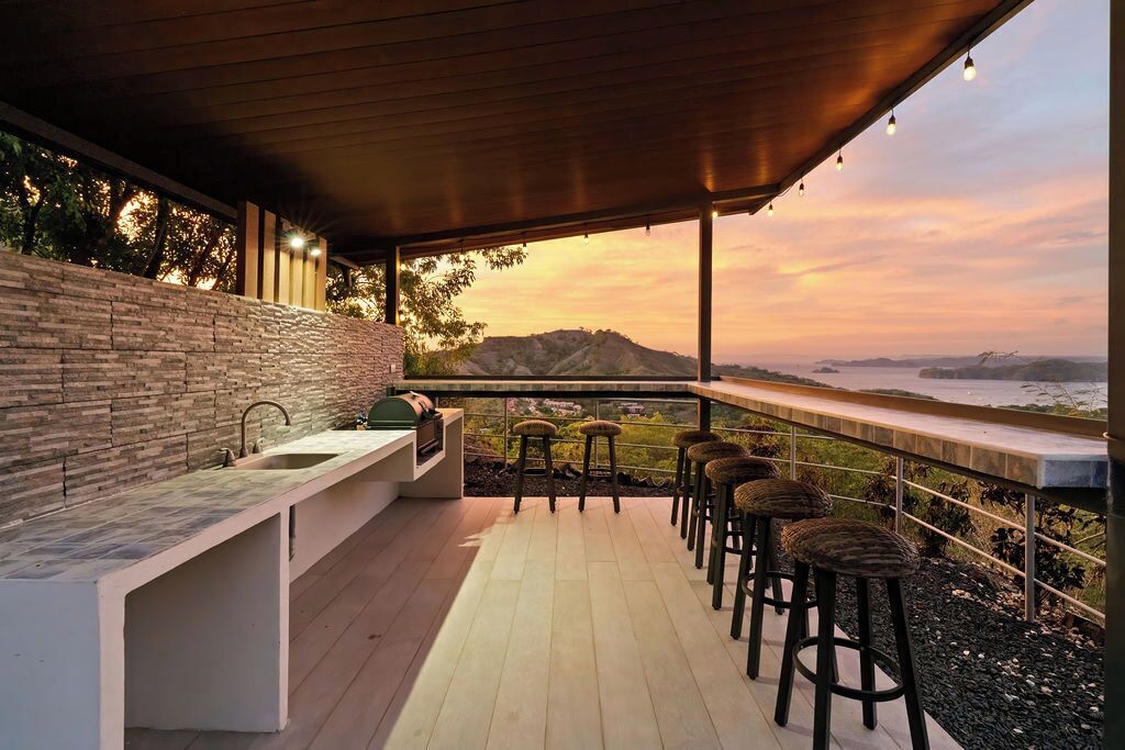 A covered outdoor bar area with a stone wall, bar stools, and a view of the landscape.
