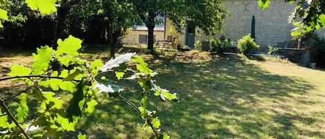 Un patio trasero con un árbol, una construcción de piedra y una zona cubierta de césped.