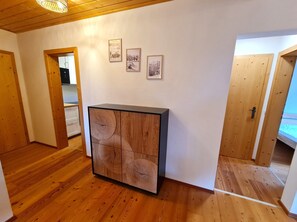Ein Zimmer mit Holzboden, einem zentralen Schrank mit Holzmaserung und drei gerahmten Bildern an der Wand.