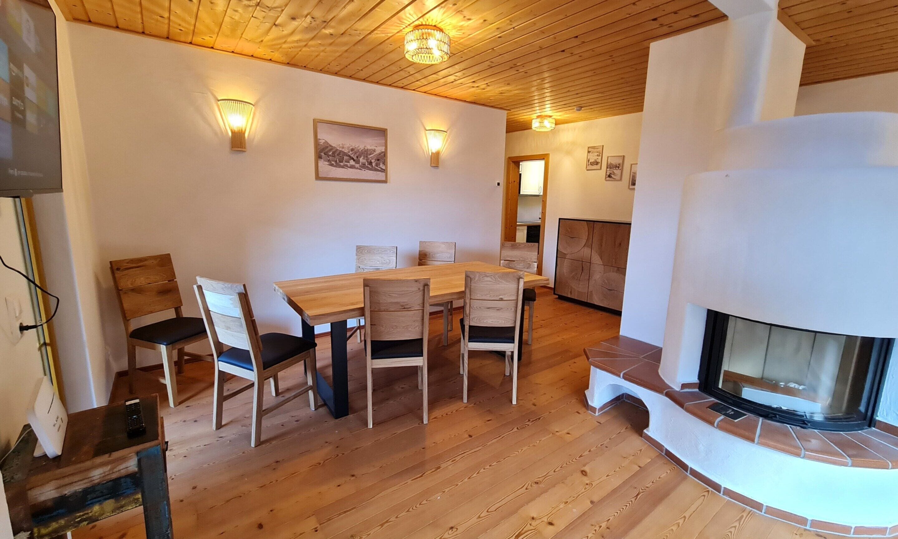 Un comedor con una mesa y sillas de madera, una chimenea e iluminación en la pared.