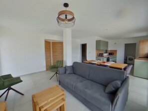 Ein modernes Wohnzimmer mit einem grauen Sofa, einem Holztisch und einem Essbereich mit Tisch und Stühlen.