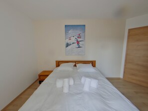 Ein ordentlich gemachtes Bett mit weißen Leinen und Handtüchern, ein hölzerner Kopfteil, ein Nachttisch mit Lampe und ein Bild von einer Seilbahn an der Wand.