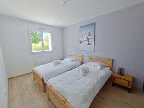 A room with two wooden beds, a window, a painting, and a bedside table. - Modern apartment, serene nature - 6 guests (Les Rousses)