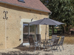 Eine Terrasse mit Tisch und Stühlen, einem großen Sonnenschirm und einem Steinhaus mit Backsteinmauer.