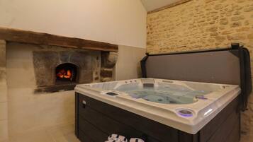 A hot tub with a stone wall and a fireplace in the background.