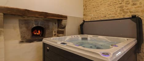 A hot tub with a stone wall and a fireplace in the background.