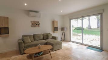 Sala de estar con sofá modular, una mesa de centro y una lámpara de pie. Hay un ventanal corredero que da a un espacio exterior.