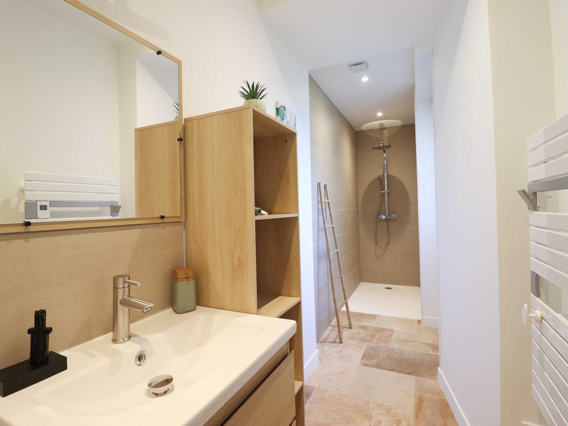 Un baño moderno con lavamanos, espejo, repisas de madera y zona de ducha.