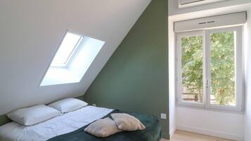Een slaapkamer met dakraam, een bed met wit beddengoed, een groene accentmuur en een raam met uitzicht op groen.