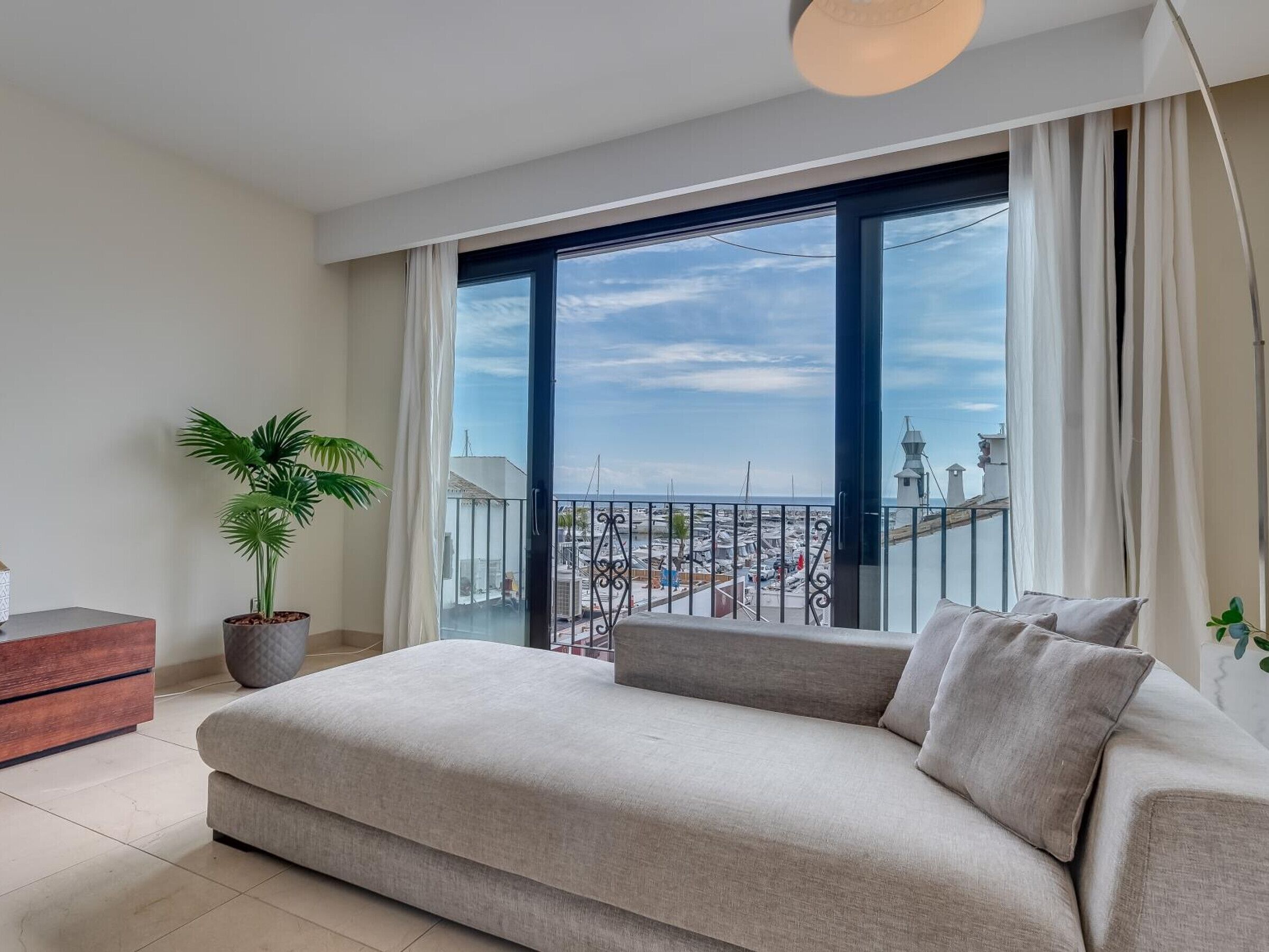 Ein modernes Wohnzimmer mit einer großen Couch, einer Topfpflanze und Blick auf eine Stadtlandschaft durch einen Balkon.