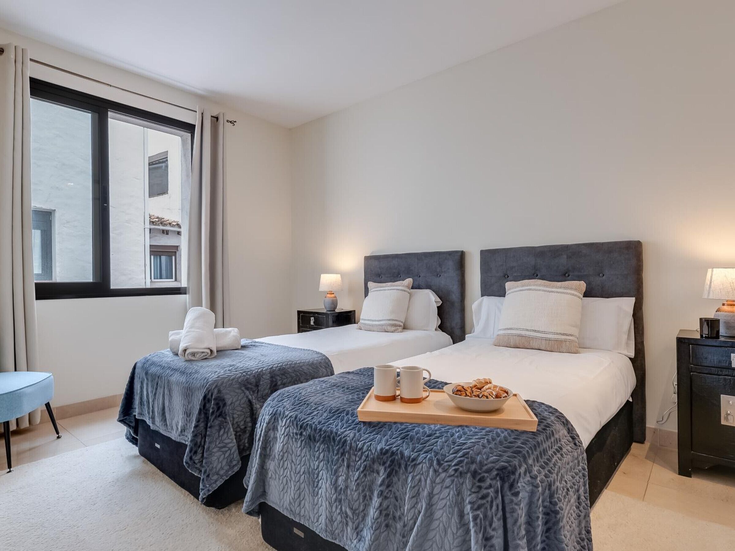 Ein Hotelzimmer mit zwei Betten, einem kleinen Tisch mit Frühstück und einem Fenster mit Vorhängen.