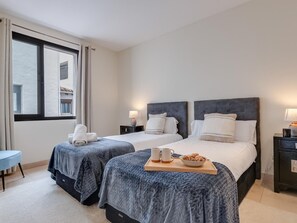 Ein Hotelzimmer mit zwei Betten, einem kleinen Tisch mit Frühstück und einem Fenster mit Vorhängen.