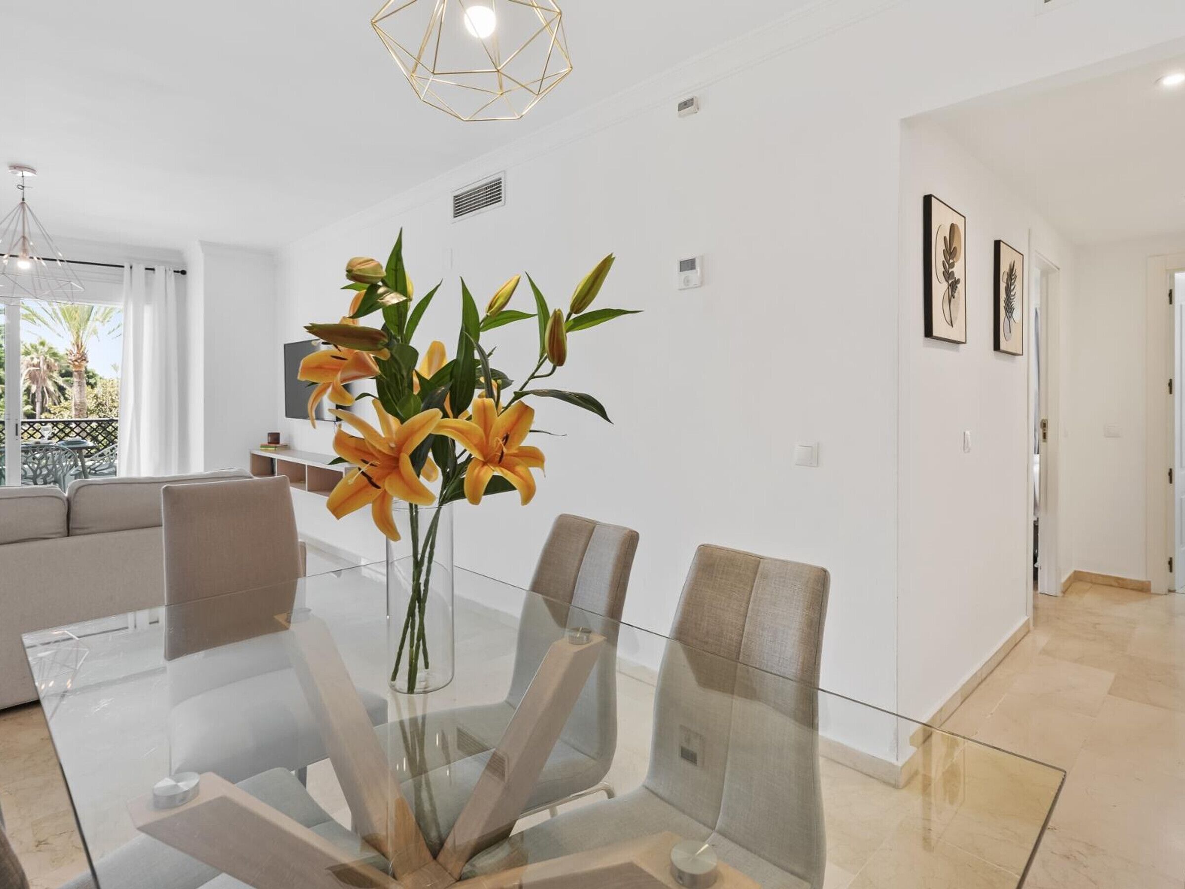 Una sala de estar moderna con una mesa de comedor de vidrio, un sofá y un jarrón decorativo con flores.