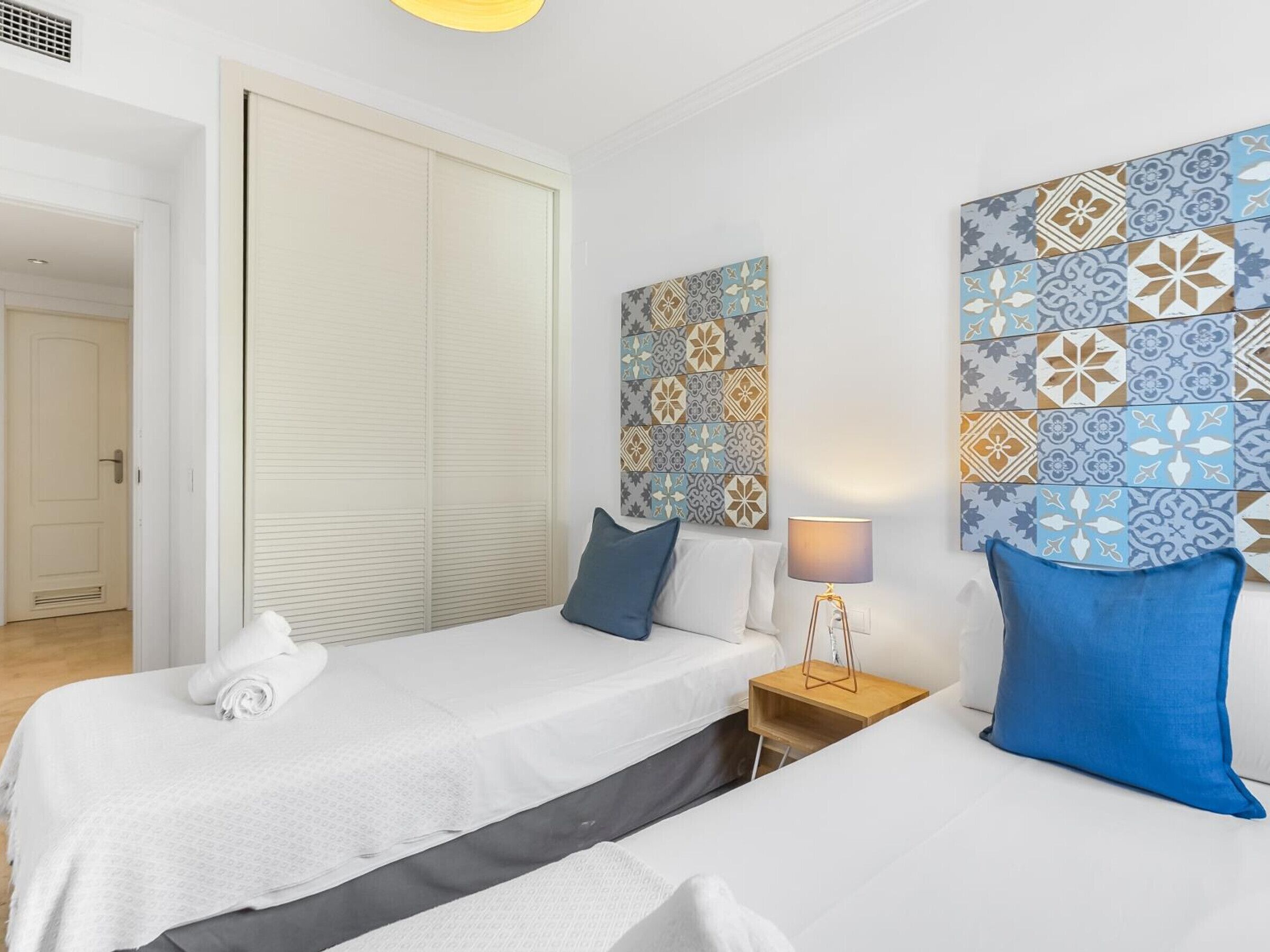 A hotel room with a bed, a bedside table, a lamp, and a wall with patterned tiles.