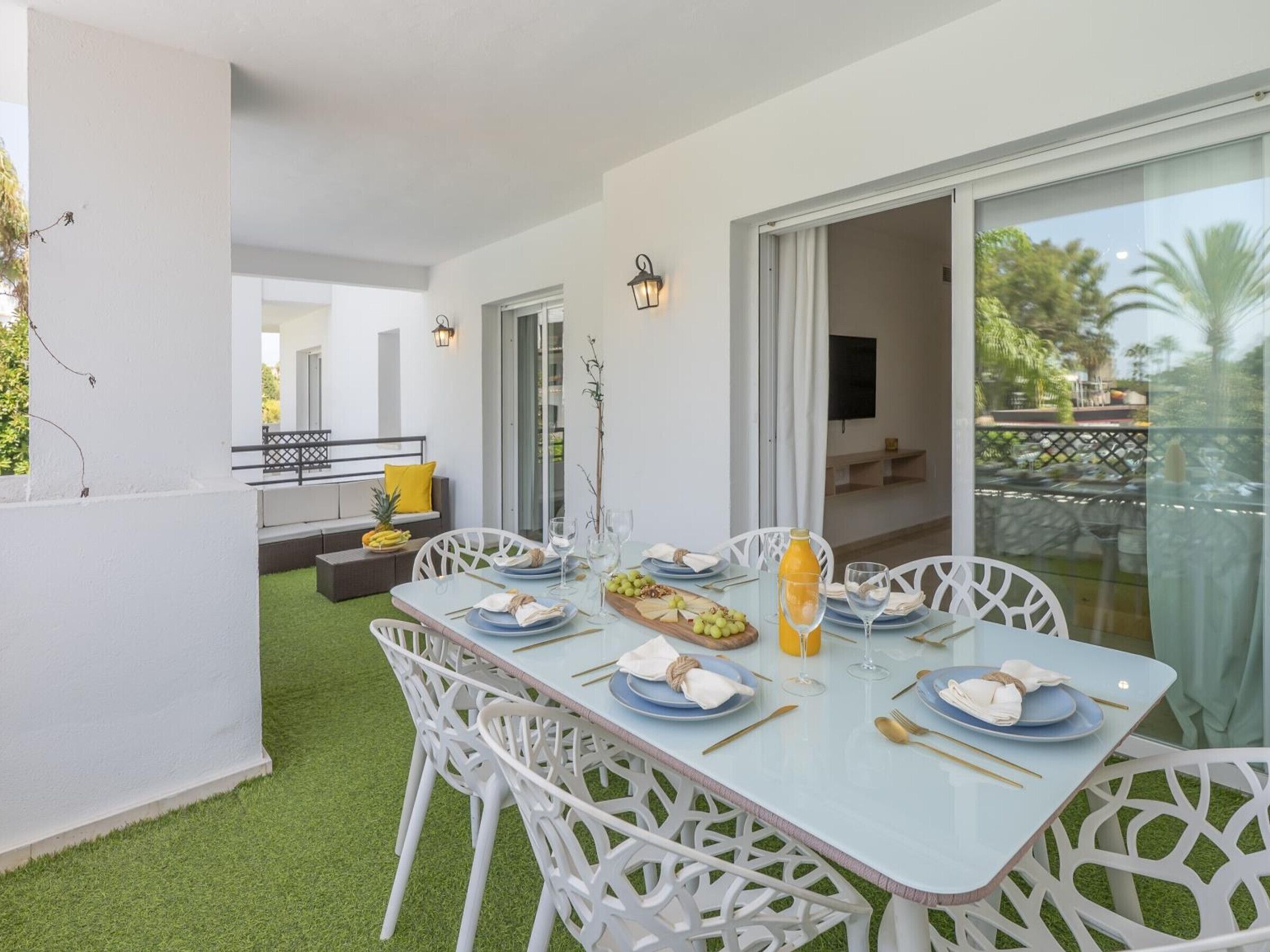 Un comedor con una mesa dispuesta para cuatro personas, rodeada de sillas blancas, con vistas al exterior.