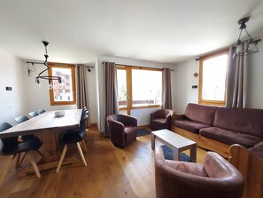 Ein modernes Wohnzimmer mit Essbereich, Holzboden und großen Fenstern.