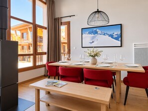 Comedor con una mesa dispuesta para cuatro, sillas rojas, un banco, un florero con flores y un cuadro en la pared.
