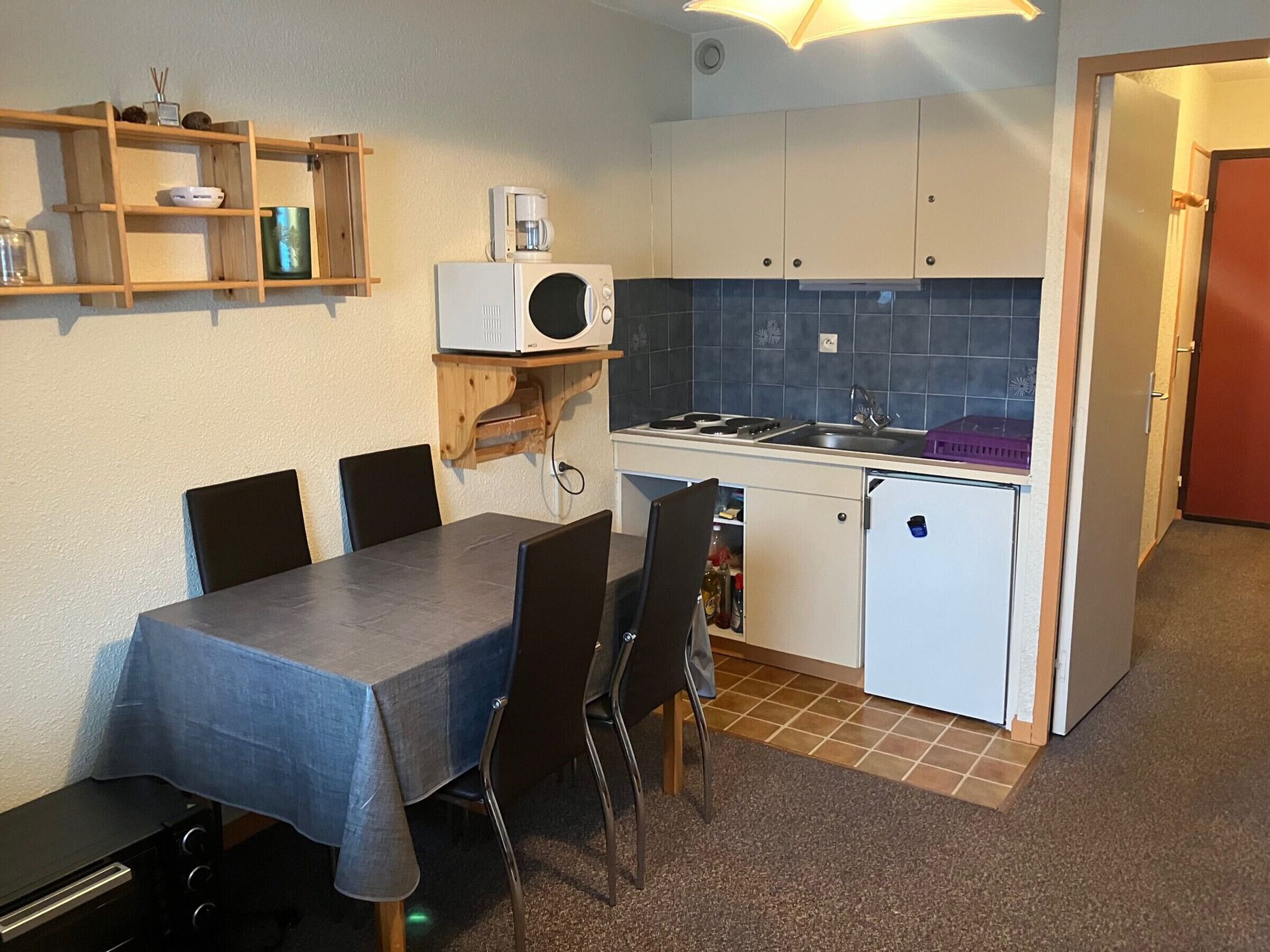 Una cocina compacta con mesa, sillas, microondas, refrigerador y lavamanos.