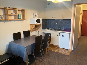 A compact kitchen with a dining table, chairs, a microwave, a refrigerator, and a sink.
