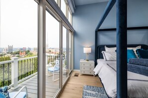 Ein Schlafzimmer mit großem Fenster, einem Bett, einem Nachttisch und einem Stuhl auf einem Balkon.