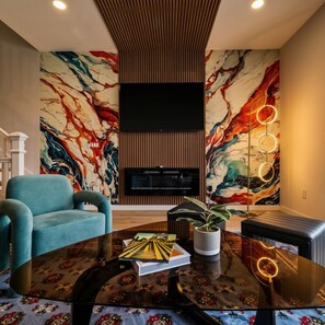 Un salon moderne comprenant un canapé, une table basse avec des livres et une plante, un téléviseur à écran plat et un mur au motif rappelant le marbre.