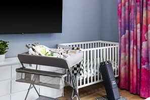 A baby changing station with a high chair, a crib, and a television mounted on the wall. - Premium Mt. Washington Retreat: VIP Views, Hot Tub, Garage (Pittsburgh)