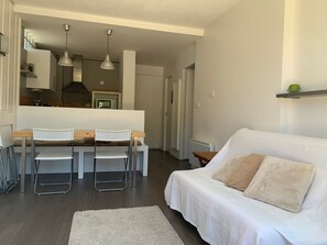 A modern living room with a white sofa, a dining table with chairs, and a kitchen area in the background. - Apartment with large terrace - 4 guests (Pra-Loup)