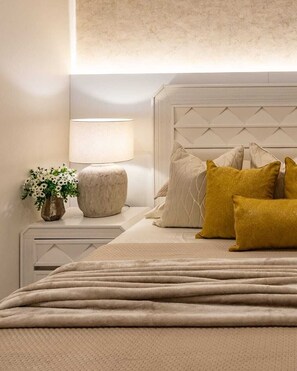 Ein ordentlich eingerichtetes Schlafzimmer mit einem Bett, Kissen, einer Nachttischlampe und einer Blumenvase.