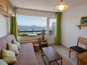 A cozy room with a sofa, a table, a chair, and a view of the outdoors. - Central studio, pets welcome - 4 guests (Saint-Michel-de-Chaillol)