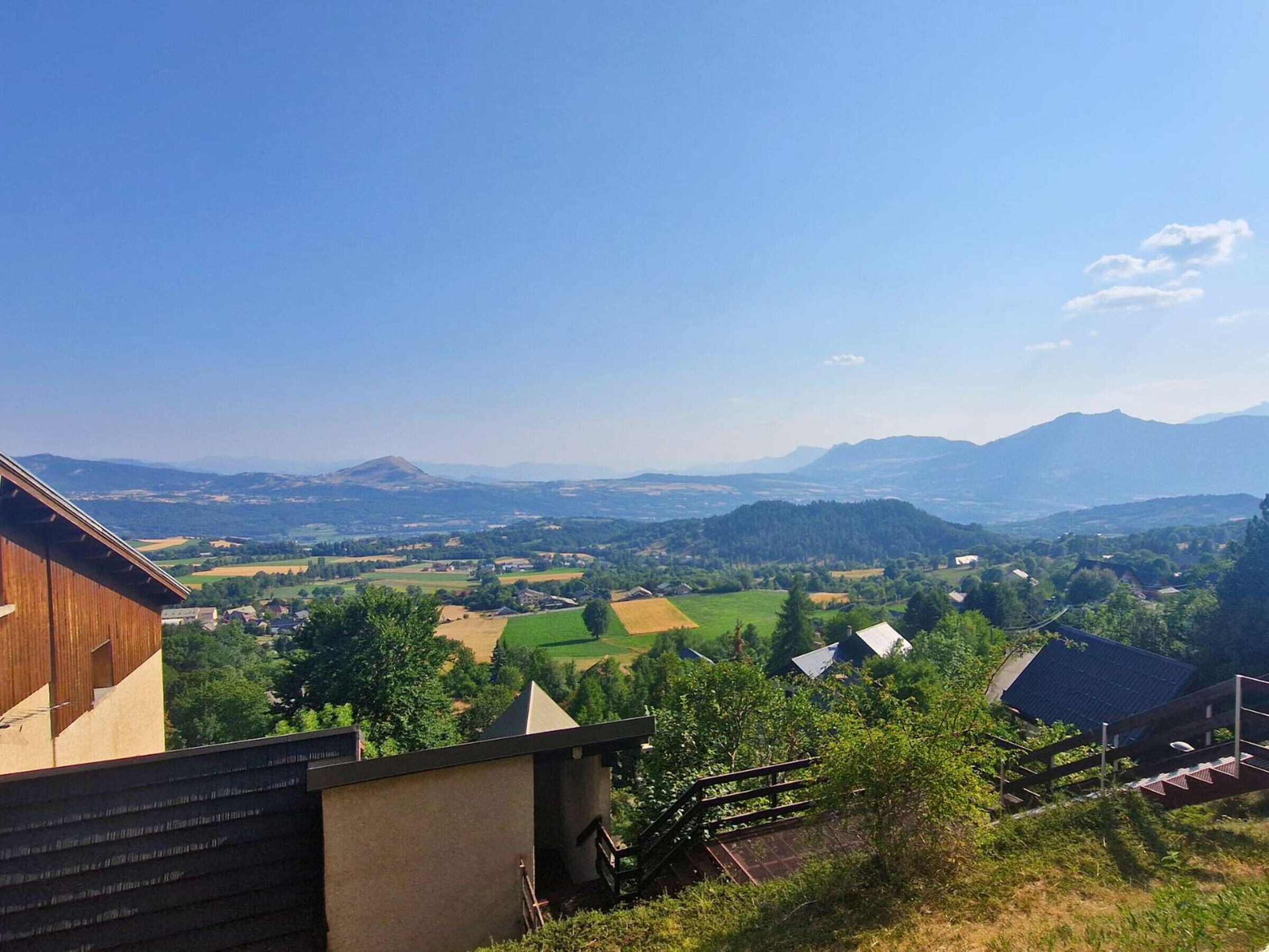 Ländliche Landschaft mit Blick auf ein Tal, Häuser und ferne Berge.