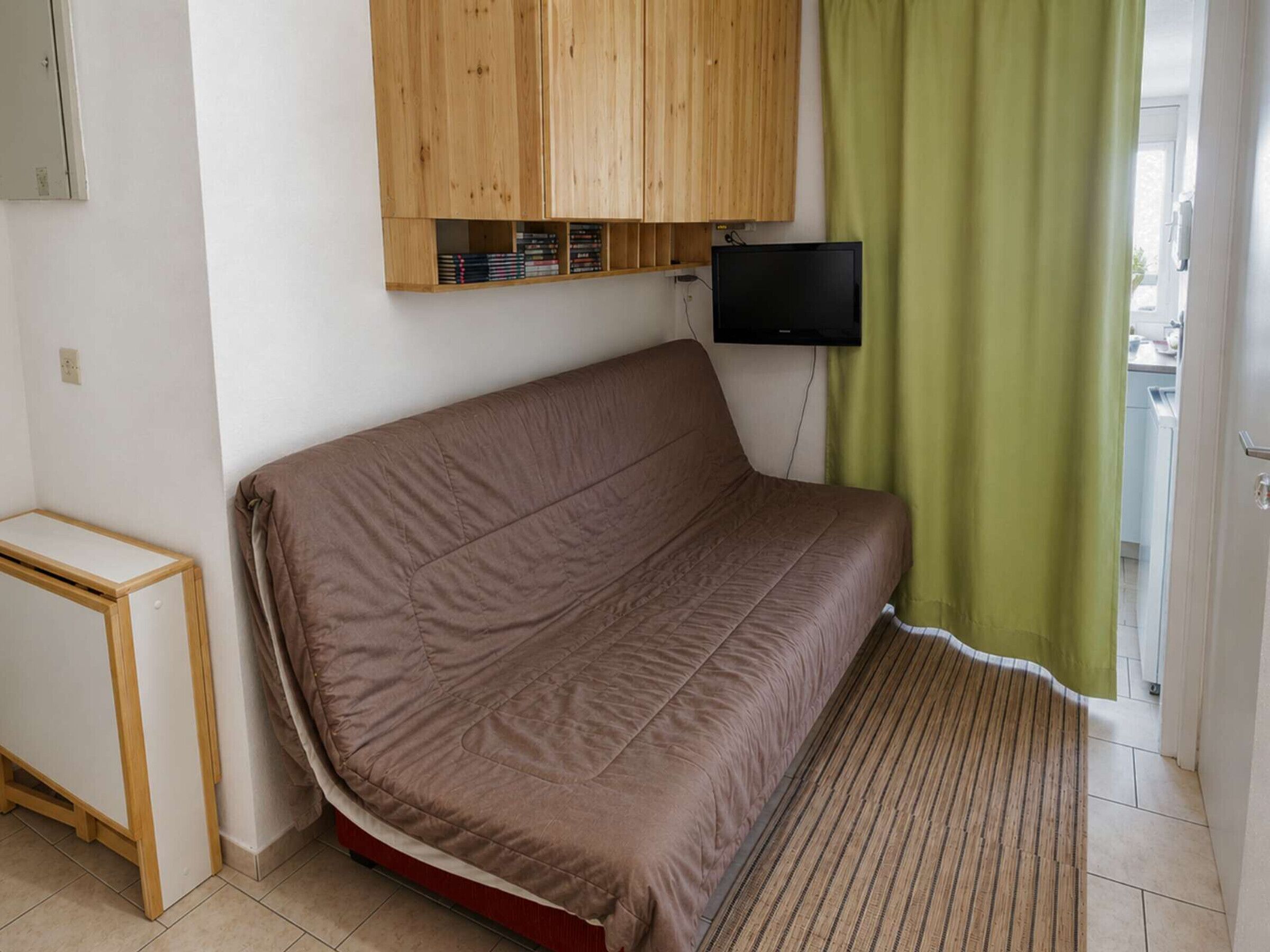 A room with a sofa, a television mounted on the wall, and a green curtain.