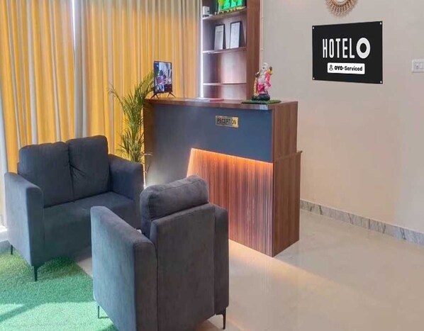 Un espace d’accueil d’hôtel comprenant un comptoir de réception, deux fauteuils, une plante en pot et un panneau indiquant que l’hôtel offre un service de qualité supérieure.